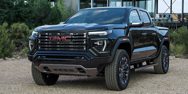 A black 2026 GMC Canyon SUV parked beside green shrubbery surrounding a glass building.