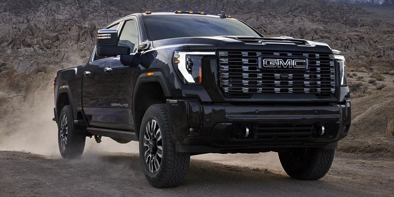 A black 2026 GMC Sierra 2500 SUV is driving up a dusty mountain road.